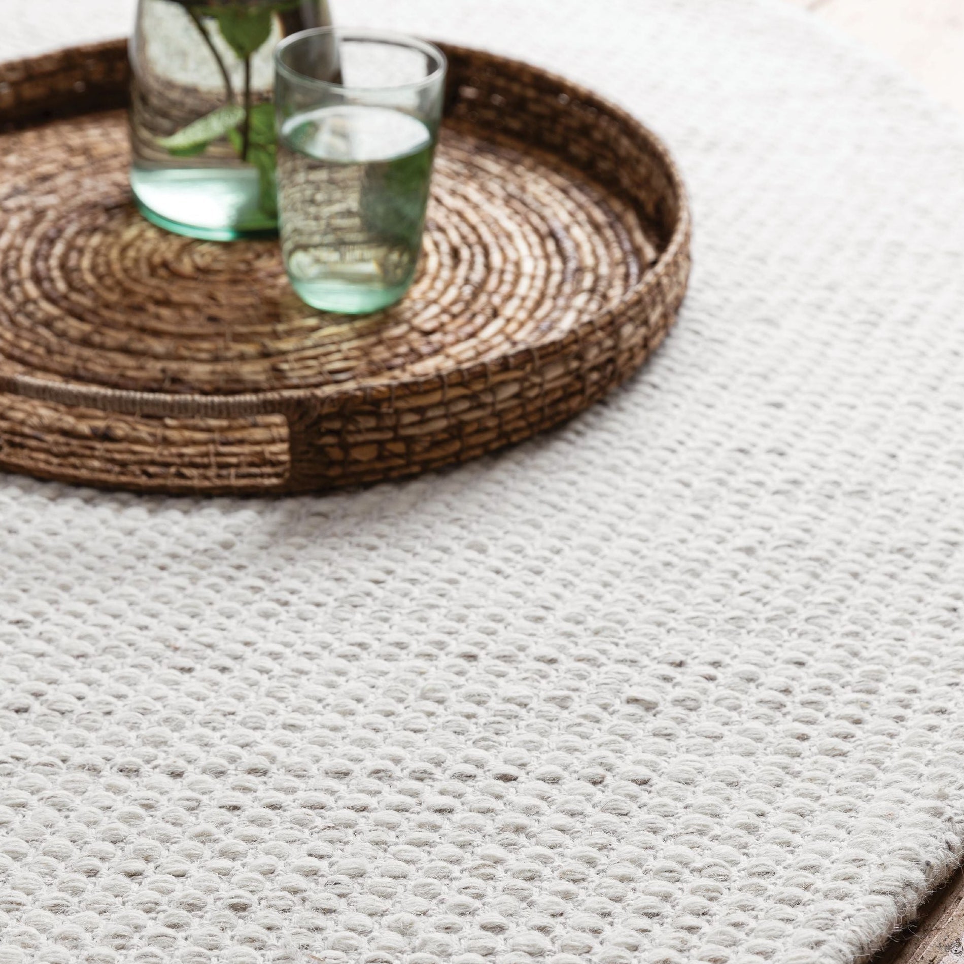 Asuri vloerkleed van MUST Living in ivoor, sfeerbeeld met rieten dienblad en glazen op de grove weving