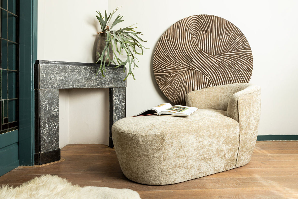 Rond houten wandpaneel boven een crèmekleurige fauteuil in een woonkamer met schouw