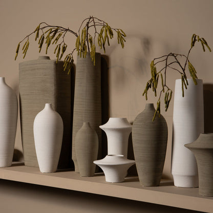 Beige Cavinn flesvaas van PTMD gestyled met een enkele tak op een houten dressoir