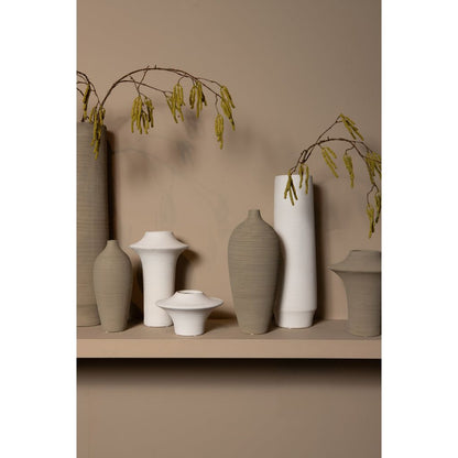 Beige Cavinn flesvaas van PTMD in een sfeerbeeld naast woonaccessoires op een kast