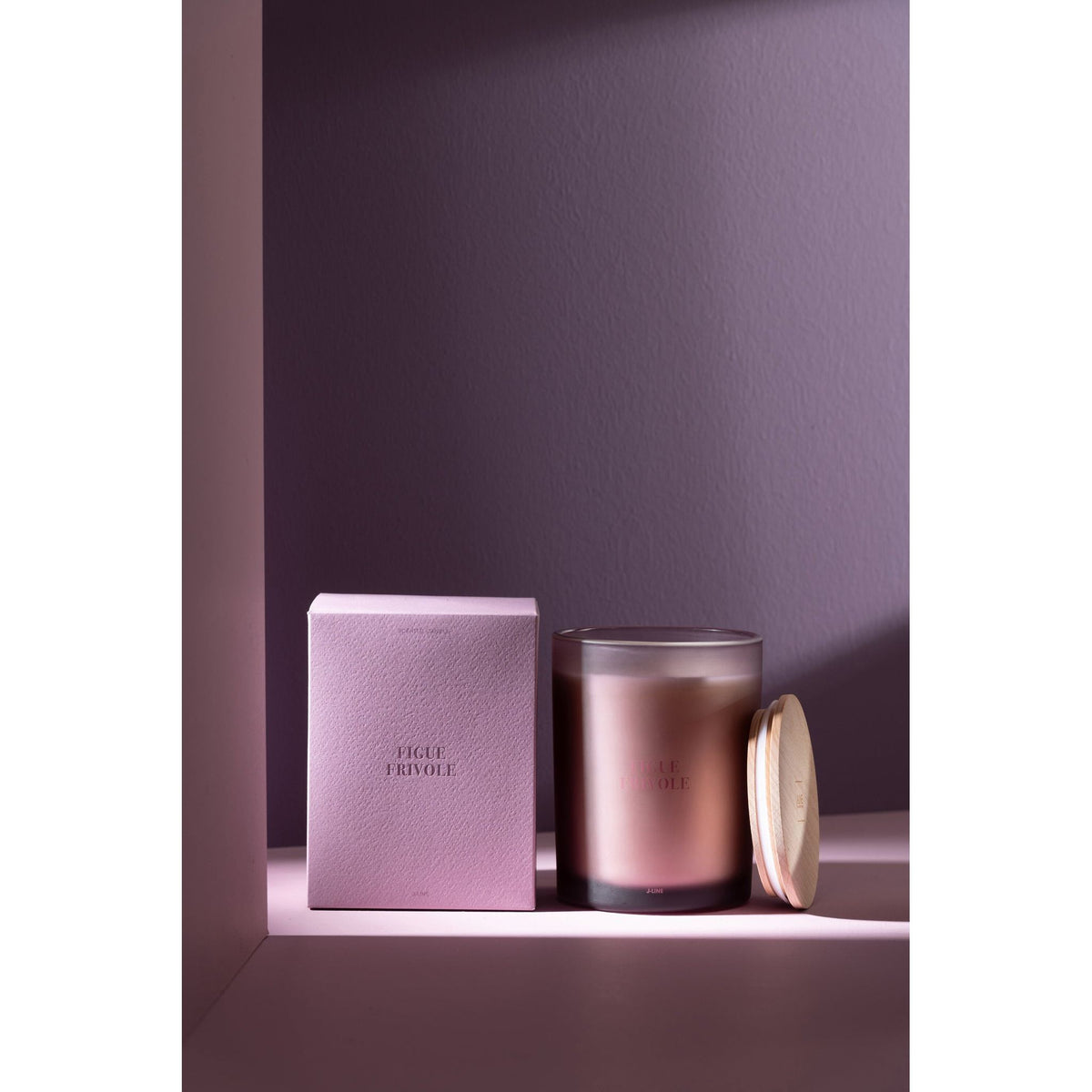 Geurkaars Accords Essentiels Figue Frivole 52 Uur van J-Line gestyled tegen een paarse wand met zacht licht