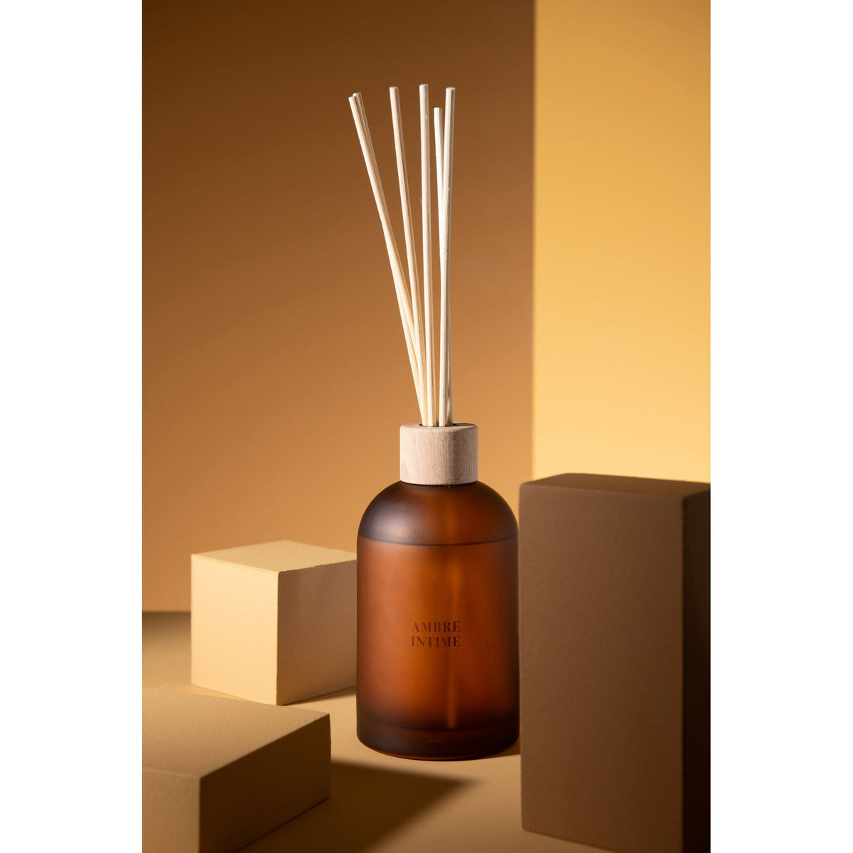 Geurstokjes Accords Essentiels Ambre Intime 550ml van J-Line met bijpassende doos in een sfeervolle okerkleurige setting