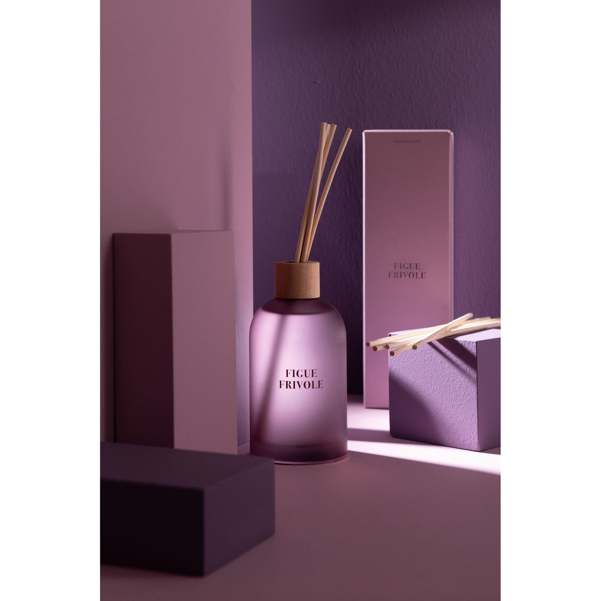 Geurstokjes Accords Essentiels Figue Frivole 250ml van J-Line gestyled tegen een paarse wand met zacht licht