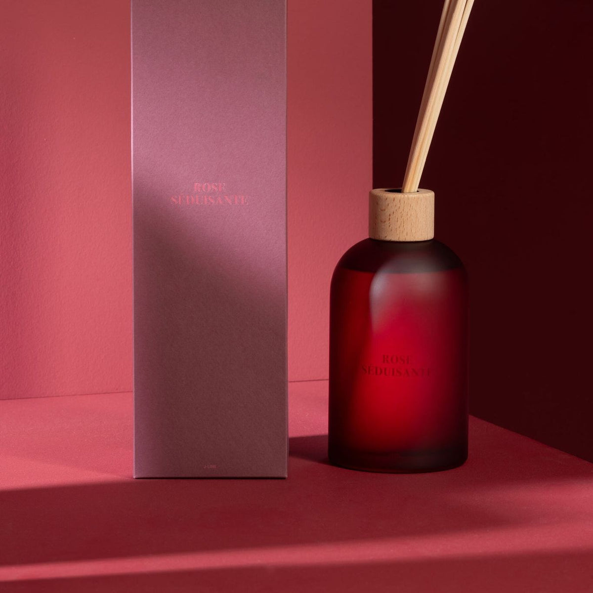Geurstokjes Accords Essentiels Rose Séduisante 550ml van J-Line met bijpassende doos in een sfeervolle rode setting