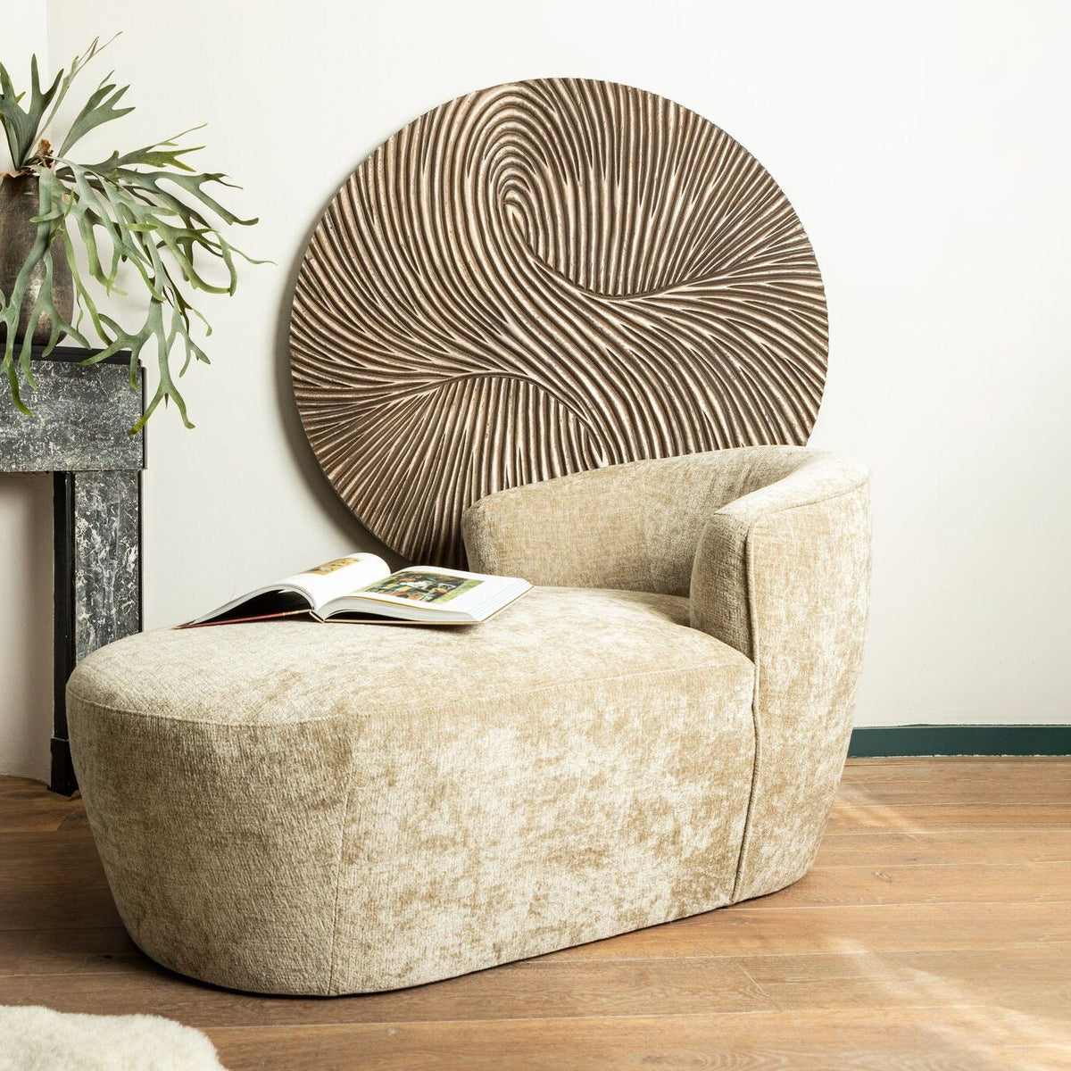 Wandpaneel Wiktor Rond Bruin Ø120cm van PTMD aan de muur boven een fauteuil naast een marmeren schouw