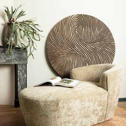 Wandpaneel Wiktor Rond Bruin Ø120cm van PTMD in een lichte woonkamer met beige fauteuil en hocker