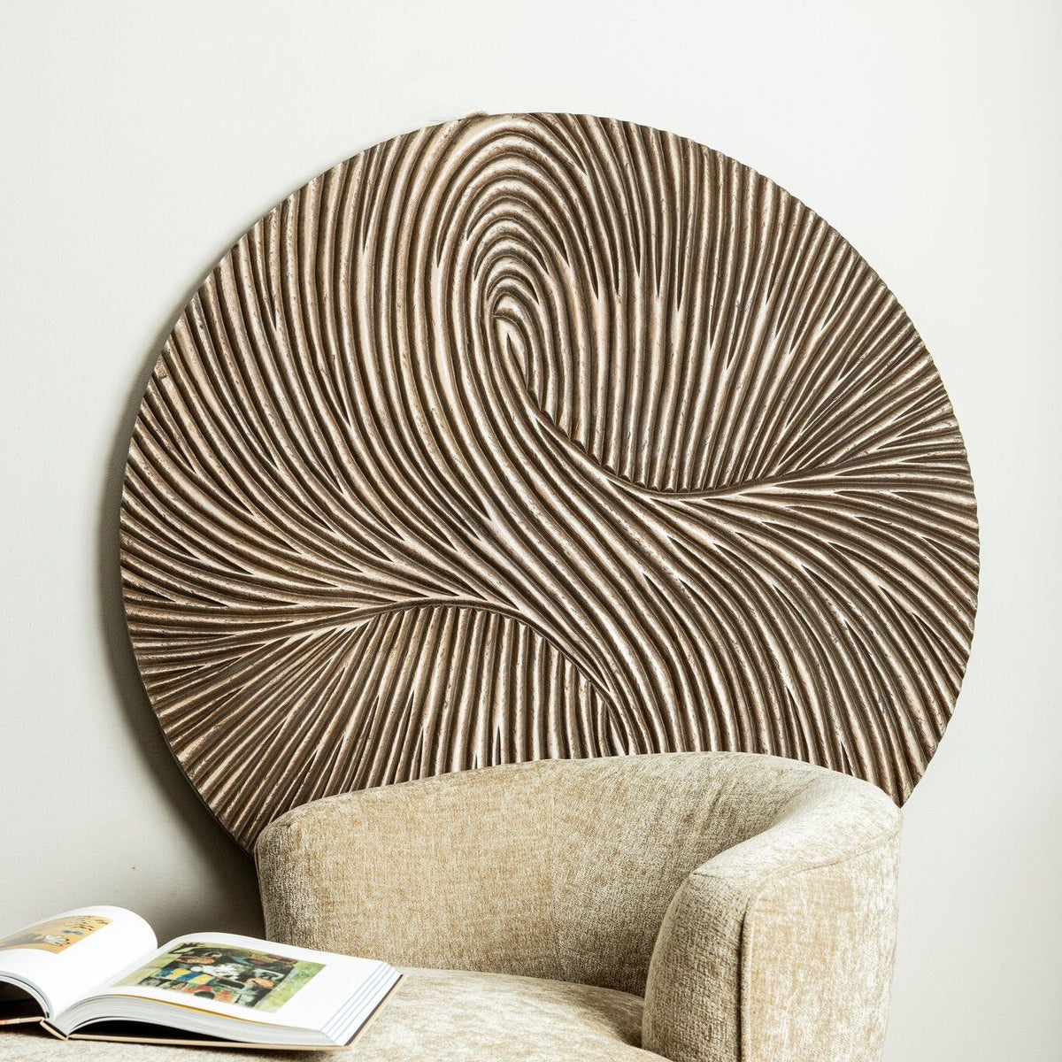 Wandpaneel Wiktor Rond Bruin Ø120cm van PTMD achter een beige fauteuil met opengeslagen boek